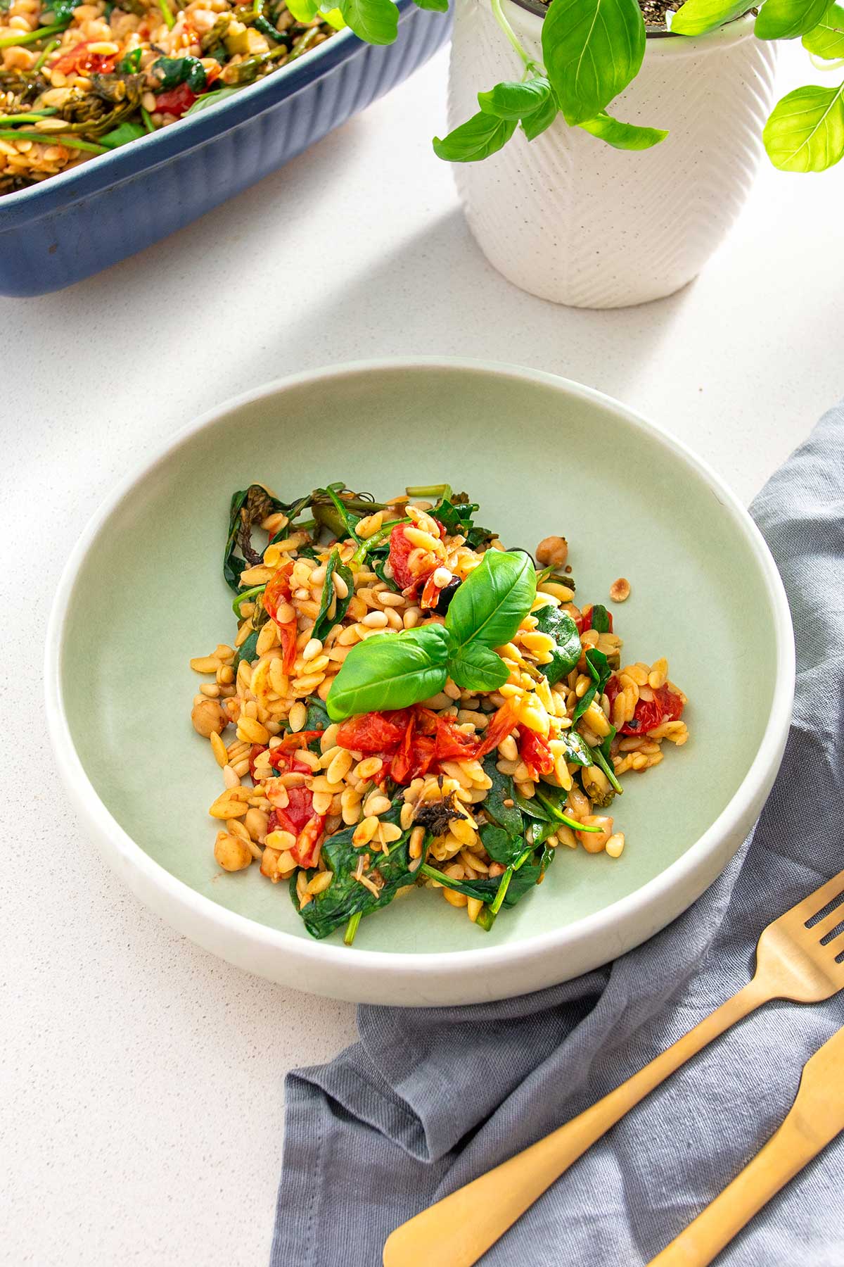 Plate of Mediterranean orzo salad with fresh spinach, tomatoes, and pine nuts, served with a gold fork and gray napkin.