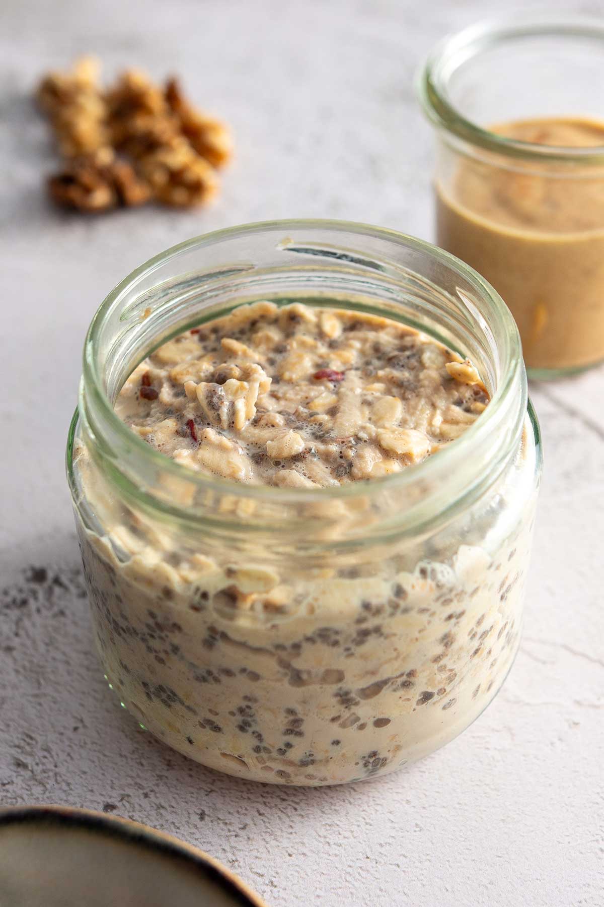 A jar of freshly prepared apple pie overnight oats before the final toppings are added, highlighting the layers of oats and chia seeds.