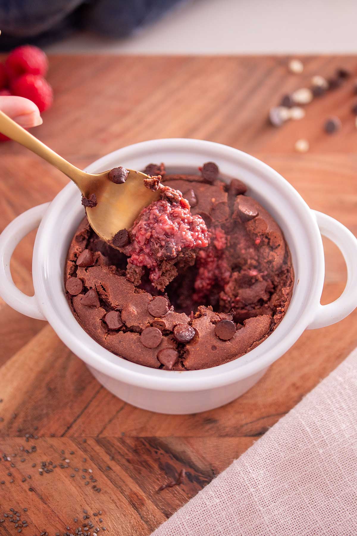 The texture of chocolate raspberry baked oats is showcased as a spoon lifts a portion, highlighting the melding of chocolate and raspberry flavors.