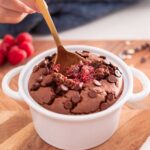 A spoon with a gold handle delves into a freshly baked dish of chocolate raspberry oats, studded with chocolate chips on top.
