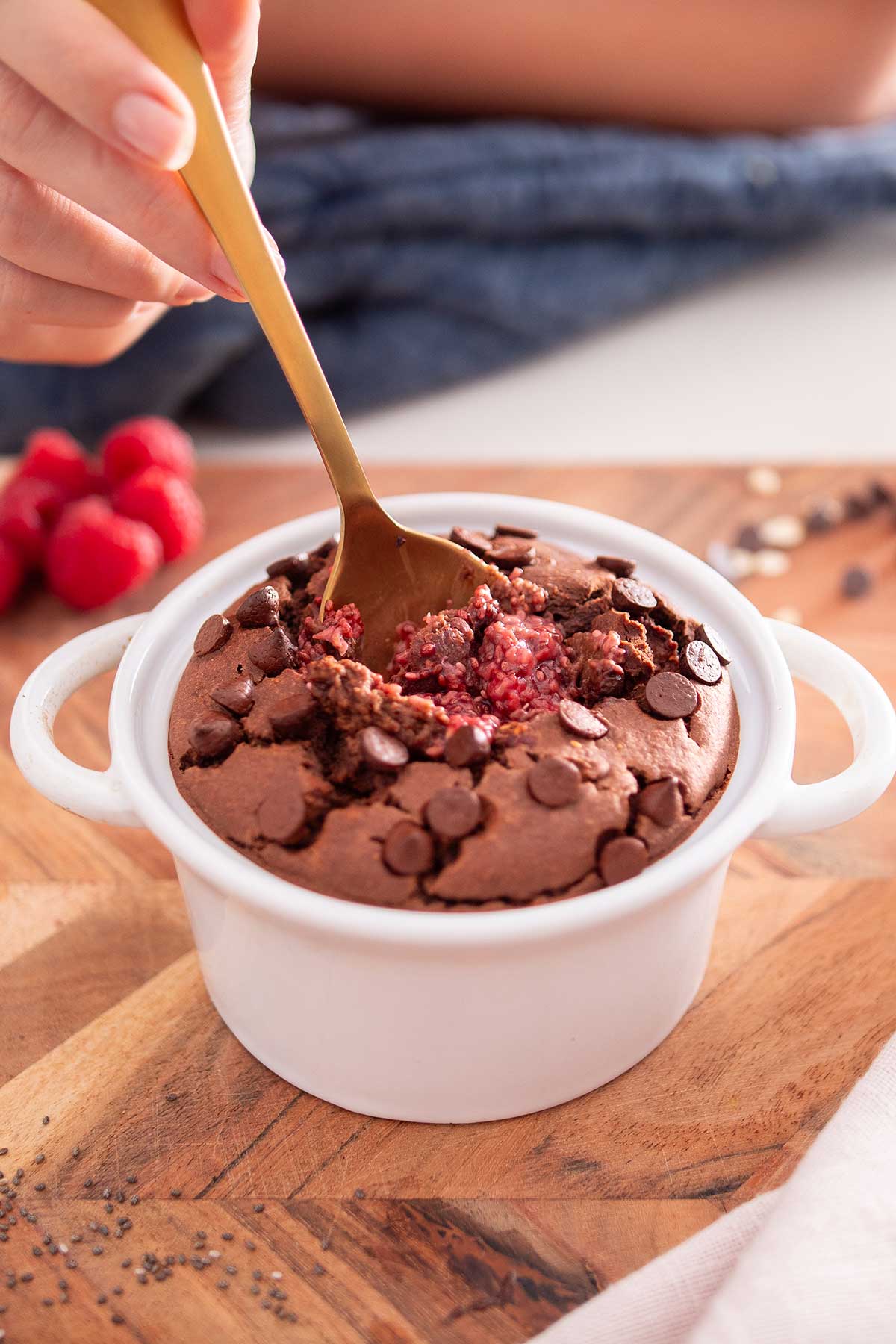 A spoon with a gold handle delves into a freshly baked dish of chocolate raspberry oats, studded with chocolate chips on top.