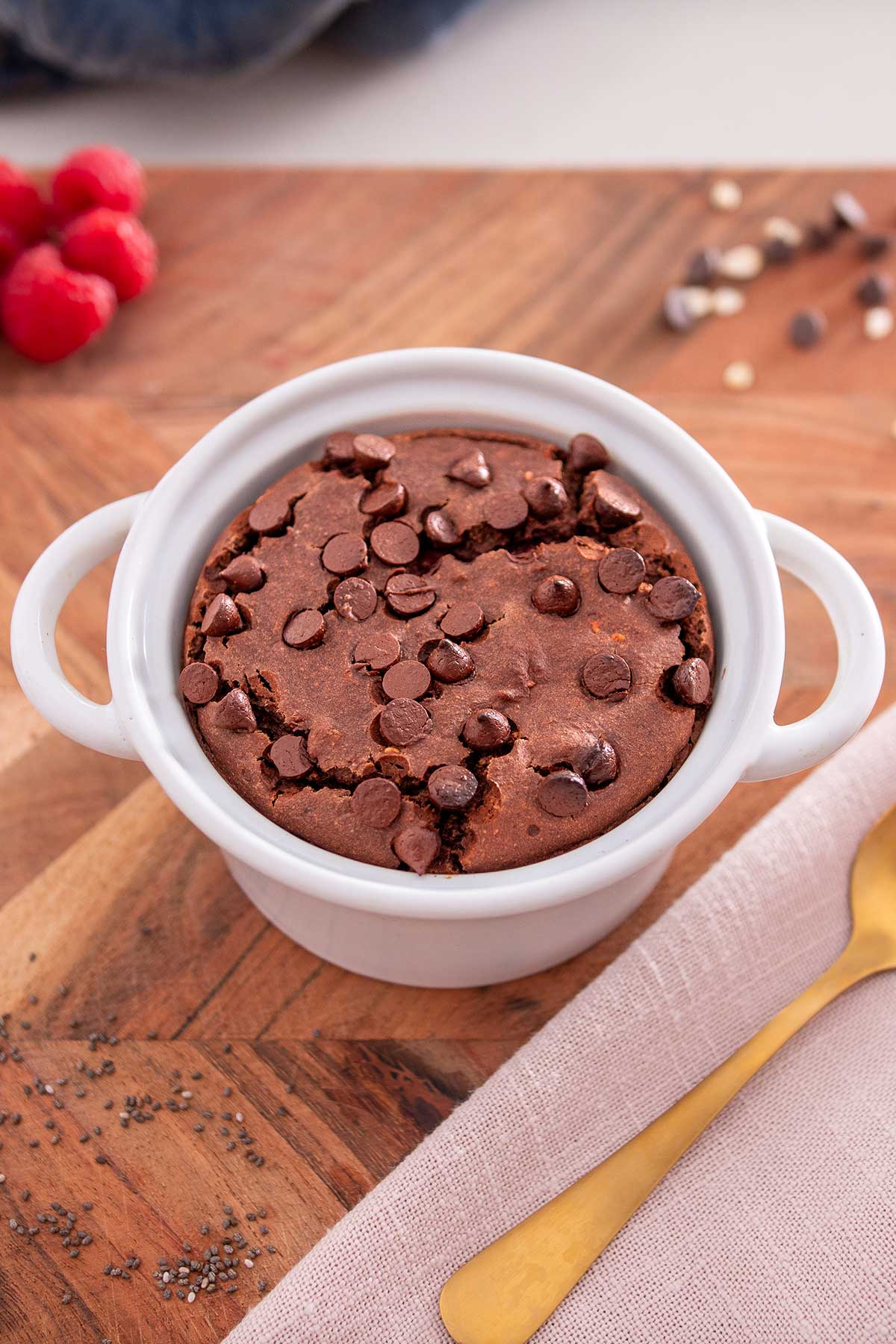A white ceramic dish filled with chocolate raspberry baked oats, chocolate chips sprinkled on top, ready to be enjoyed, with a gold spoon resting on the side.
