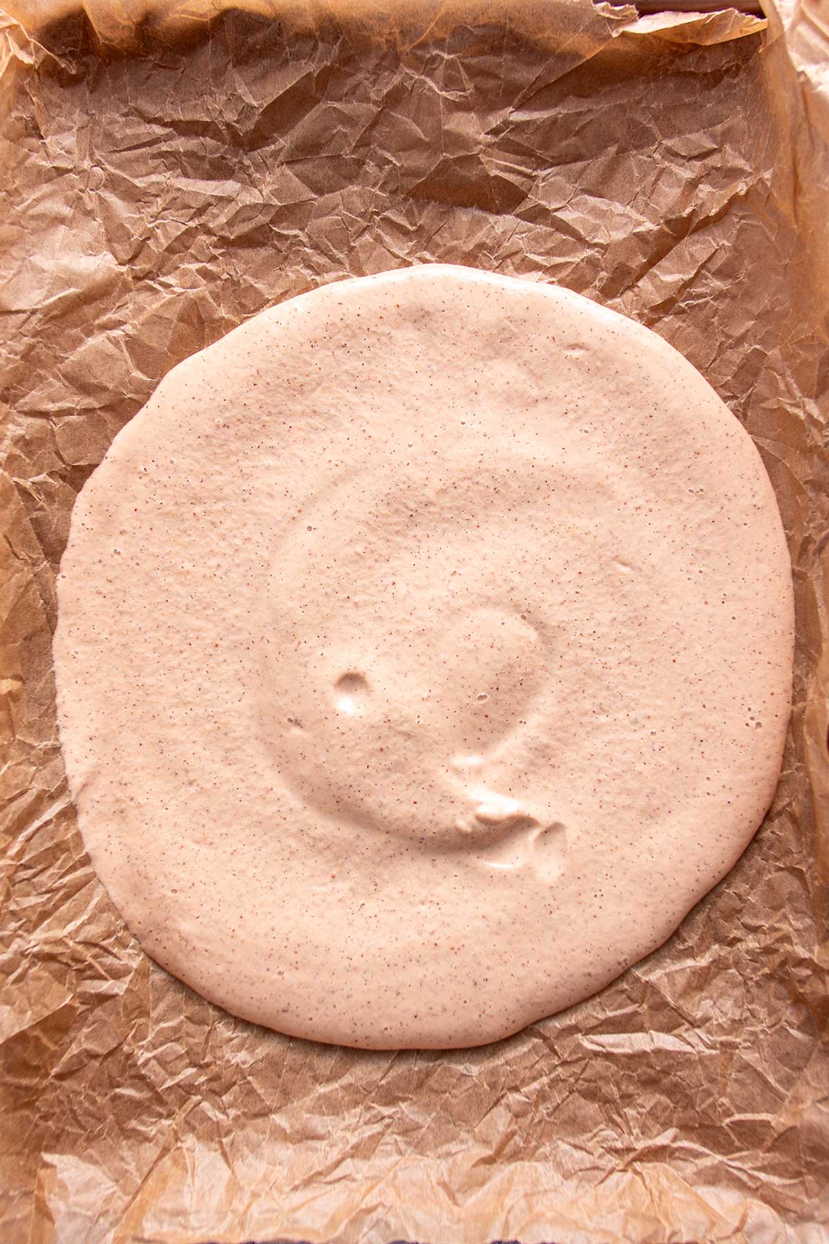 A smooth, uncooked gluten-free pizza crust batter spread on parchment paper, displaying a uniform texture and color, ready to be baked to perfection.