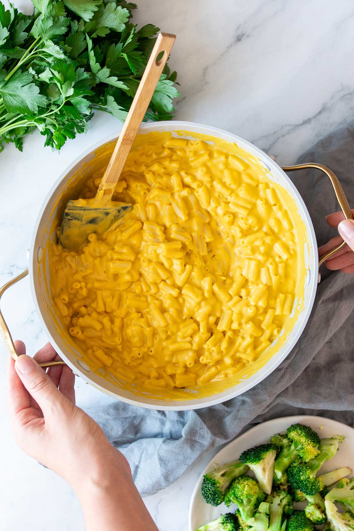 Nutritionist, Sarah Cobacho stirring a large white pot full of vegan high-protein mac and cheese, with a side of grilled broccoli on a white plate.