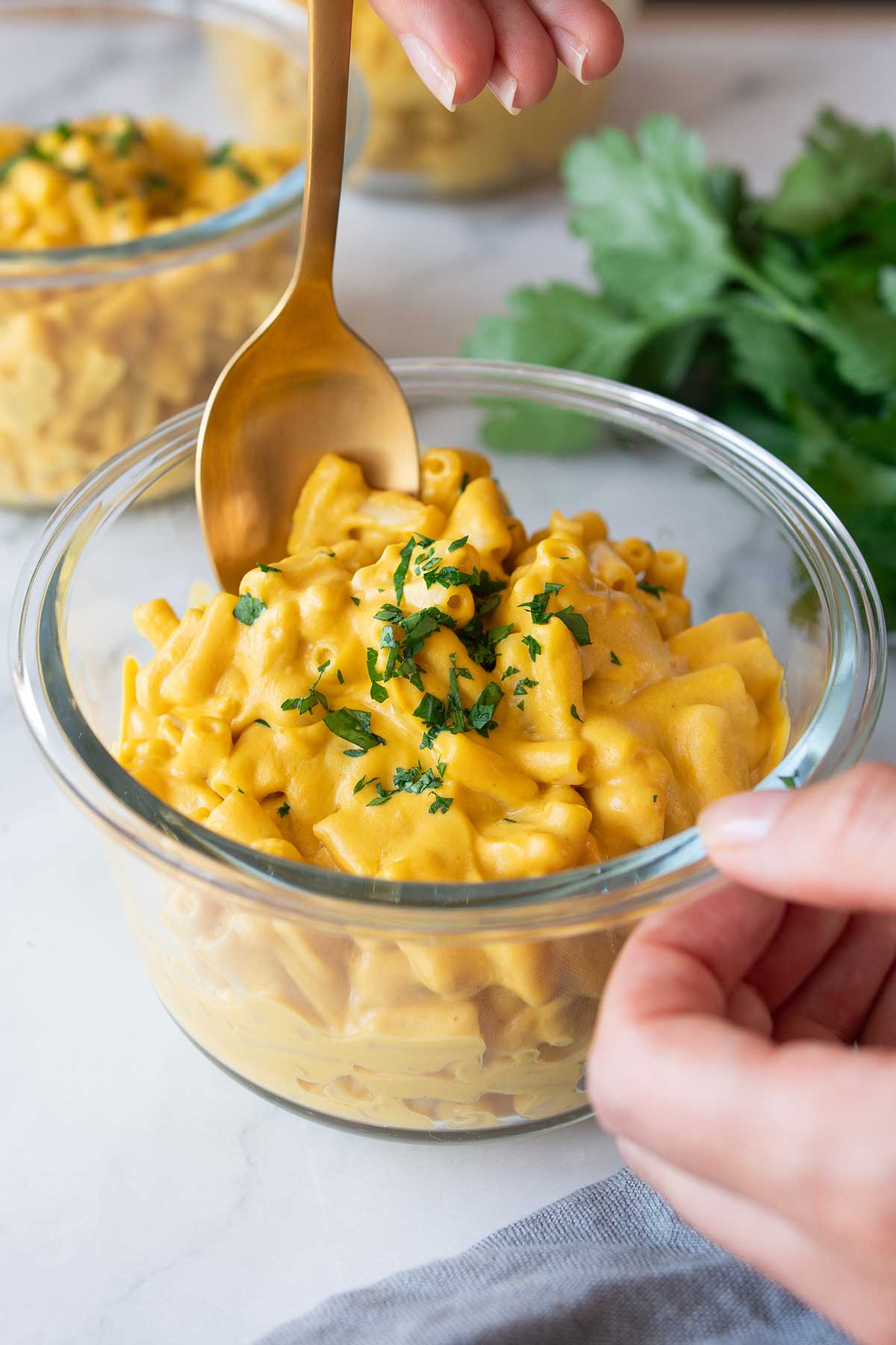 A glass bowl of vegan high-protein mac and cheese on a marble countertop, with a gold spoon, ready to be served.