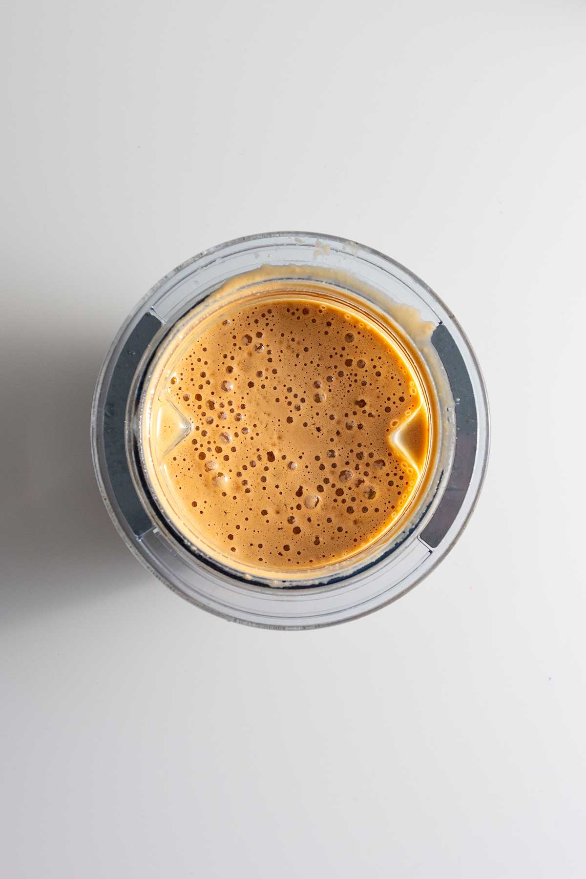 A golden-hued peanut dressing in a glass blender, its smooth texture promising a deliciously rich taste.