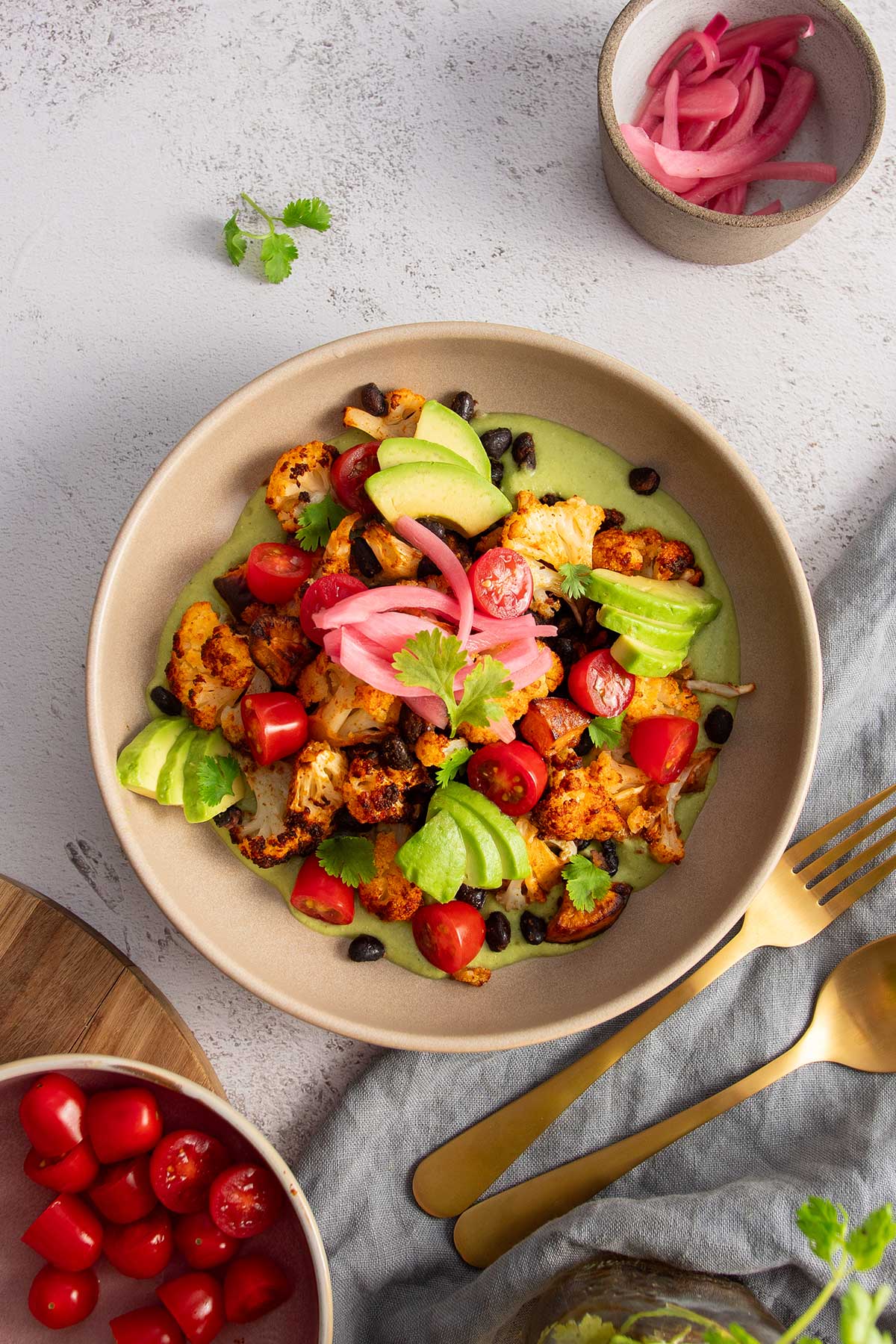 A beautifully plated roasted sweet potato and cauliflower bowl, ready to serve, featuring creamy cilantro sauce and fresh garnishes.