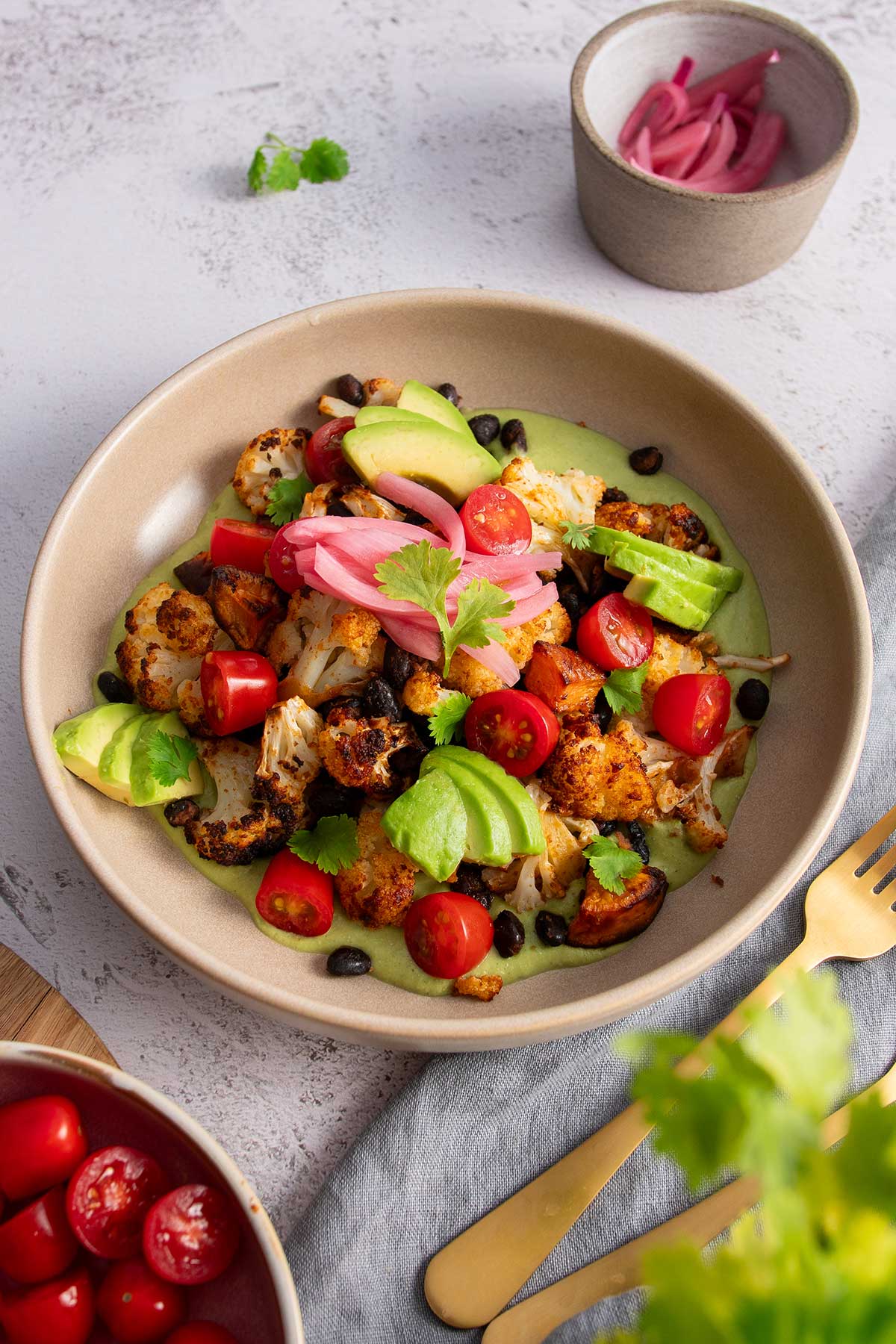 A top-down view of a roasted sweet potato and cauliflower bowl on a textured white background, highlighting the vibrant colors of the fresh ingredients