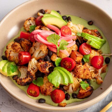Close-up of a hearty, plant-based meal of roasted sweet potato and cauliflower with creamy cilantro sauce, perfect for a healthy lunch or dinner.