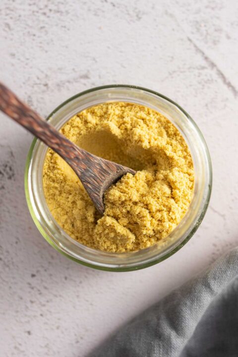 Above photo of a glass jar filled with vegan parmesan being stirred by a wooden spoon