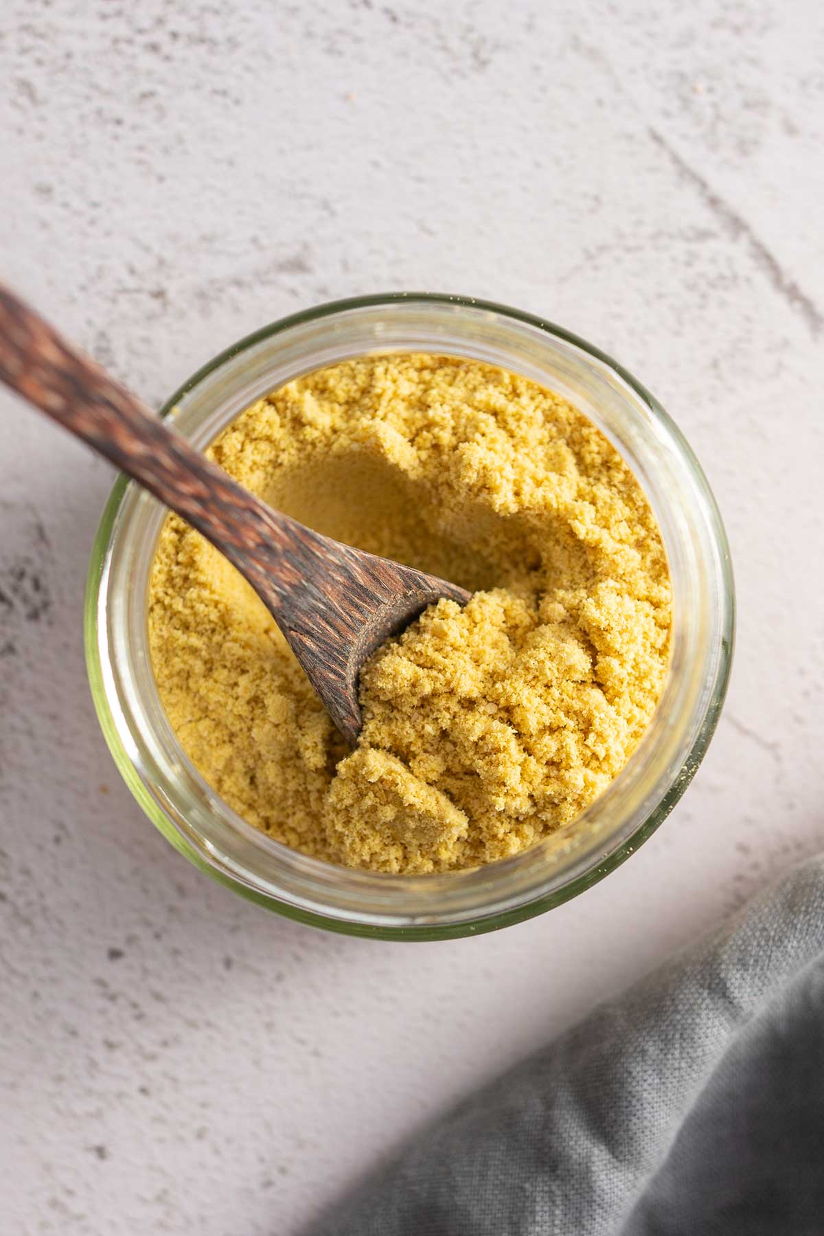 Above photo of a glass jar filled with vegan parmesan being stirred by a wooden spoon