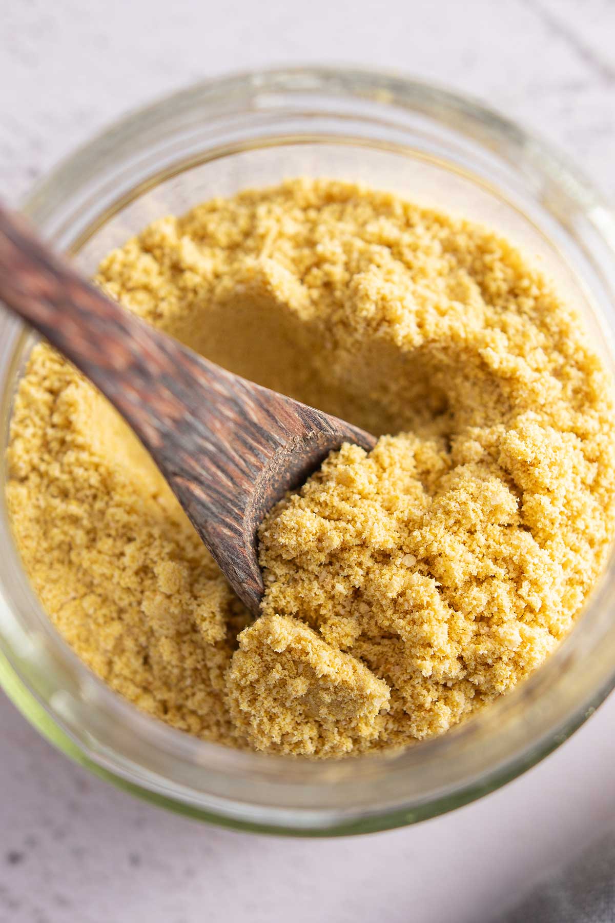 Close up photo of a glass jar filled with vegan parmesan being stirred by a wooden spoon