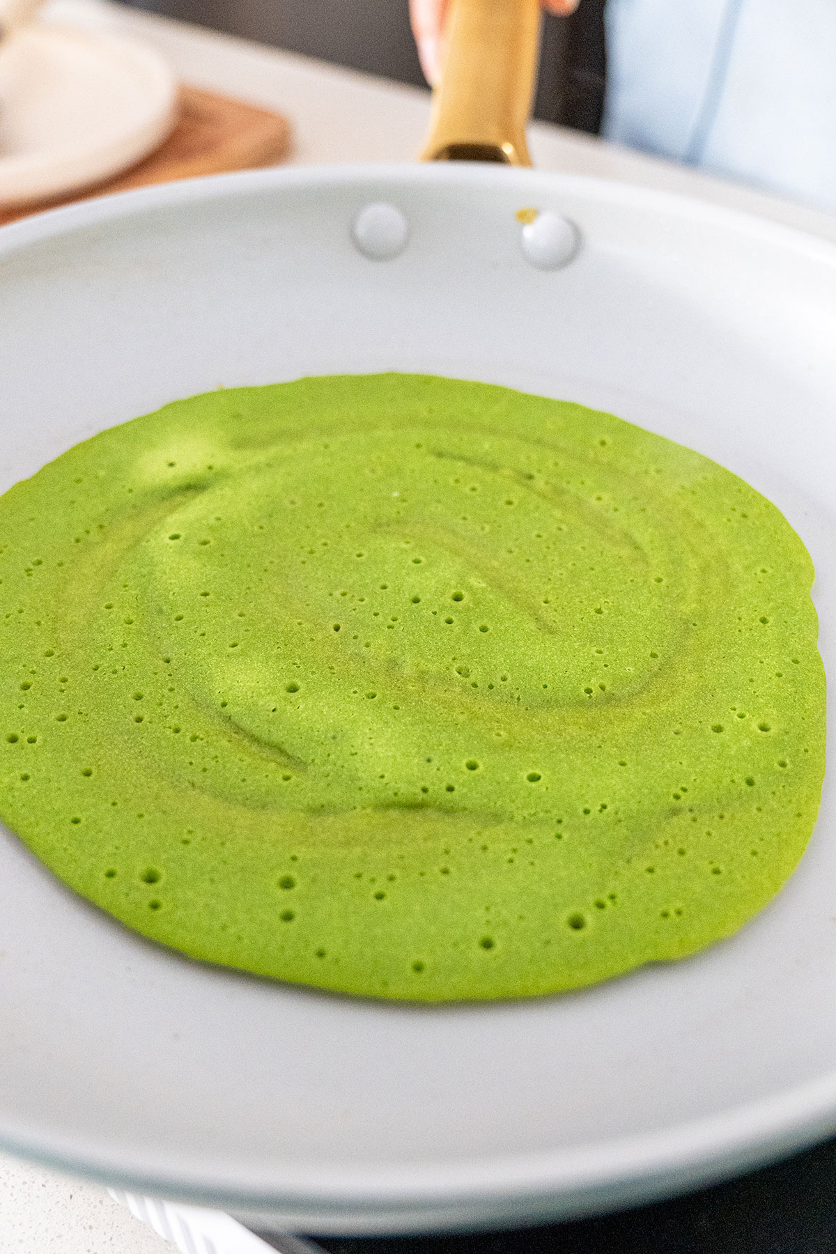 Image capturing the cooking process of a green buckwheat spinach wrap in a non-stick pan, highlighting the even spread and bubbling texture.