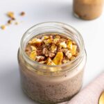 Close-up of creamy Banoffee Chia Pudding in a jar, topped with golden brown dehydrated bananas and a dusting of cacao, showcasing the layers and texture.