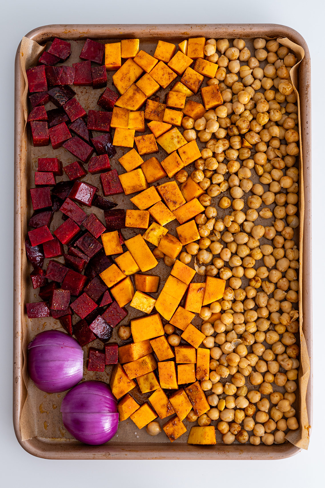 Vegetables and chickpeas arranged on parchment paper on a baking tray ready to go into the oven for Harissa Pumpkin Salad.