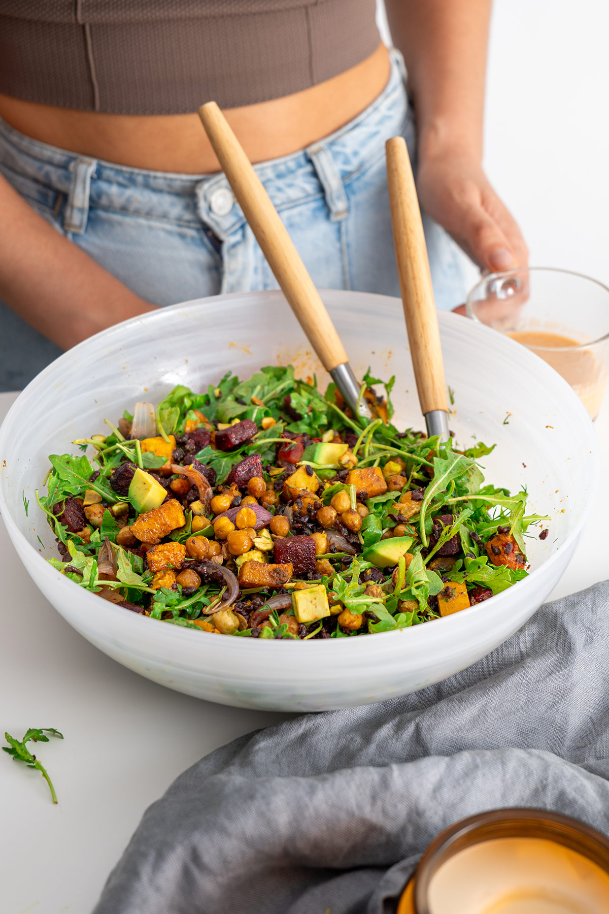 Harissa Pumpkin Salad ready to be served in a white bowl alongside glass with healthy salad dressing.
