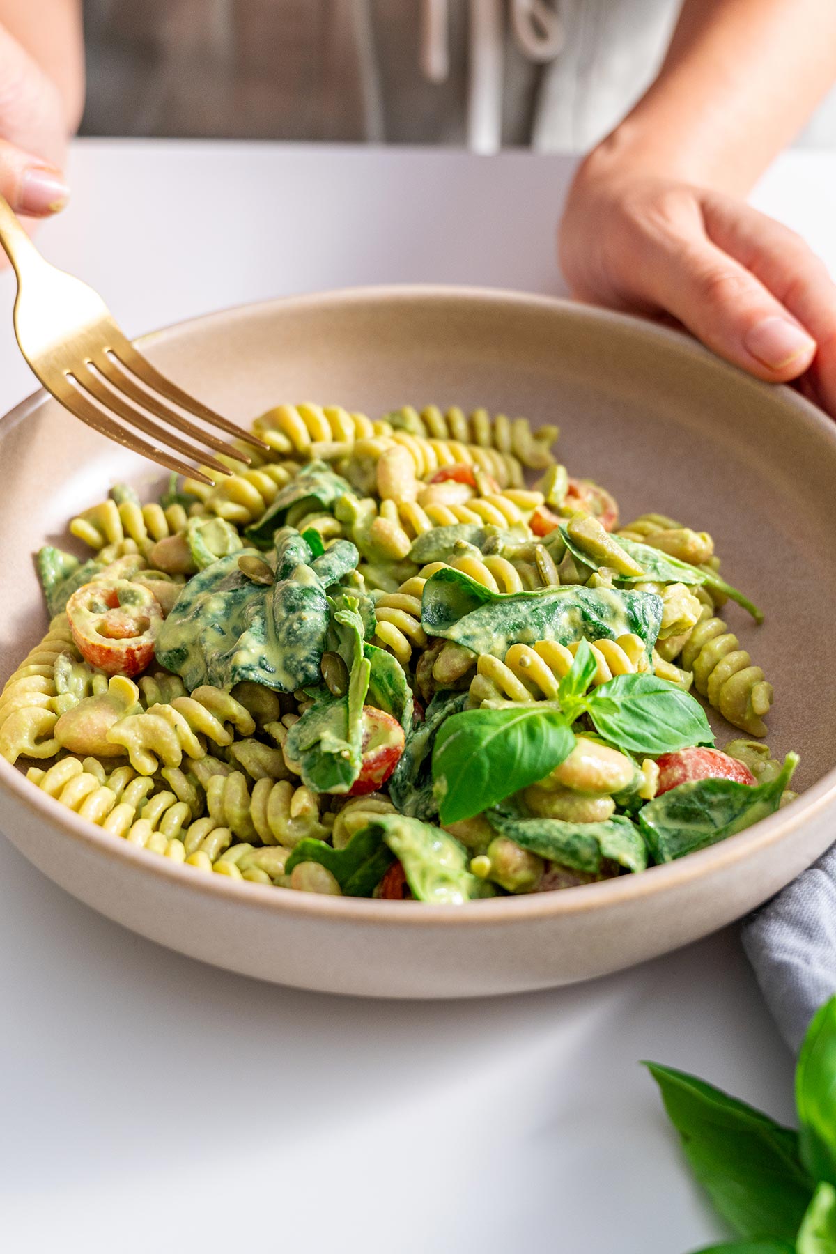 Final prepared serving of Pistachio Pesto Pasta Salad in a bowl, showcasing the creamy green pesto coating the pasta, with tomatoes, greens, and seeds on top, ready to be enjoyed.