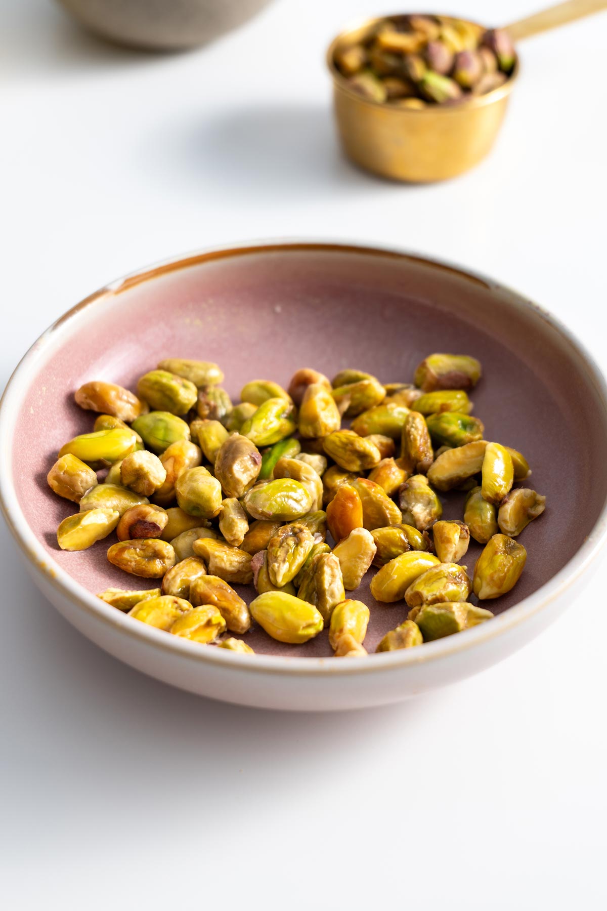 Close-up of shelled pistachios in a round pink bowl, the key ingredient for the creamy pesto, displayed with rich texture and color variation.