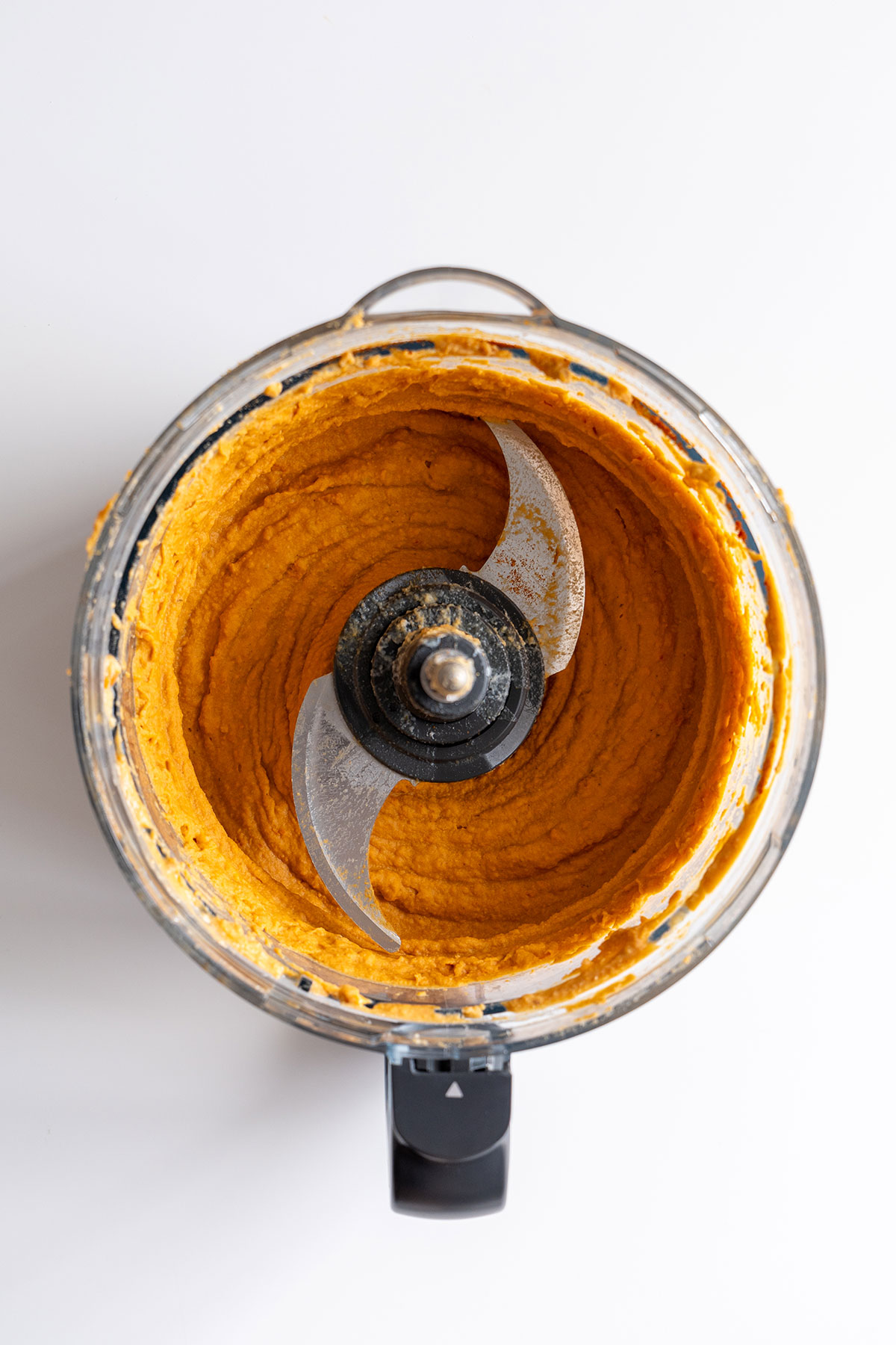A food processor containing freshly made red lentil hummus, showcasing a vibrant orange hue and a creamy texture.