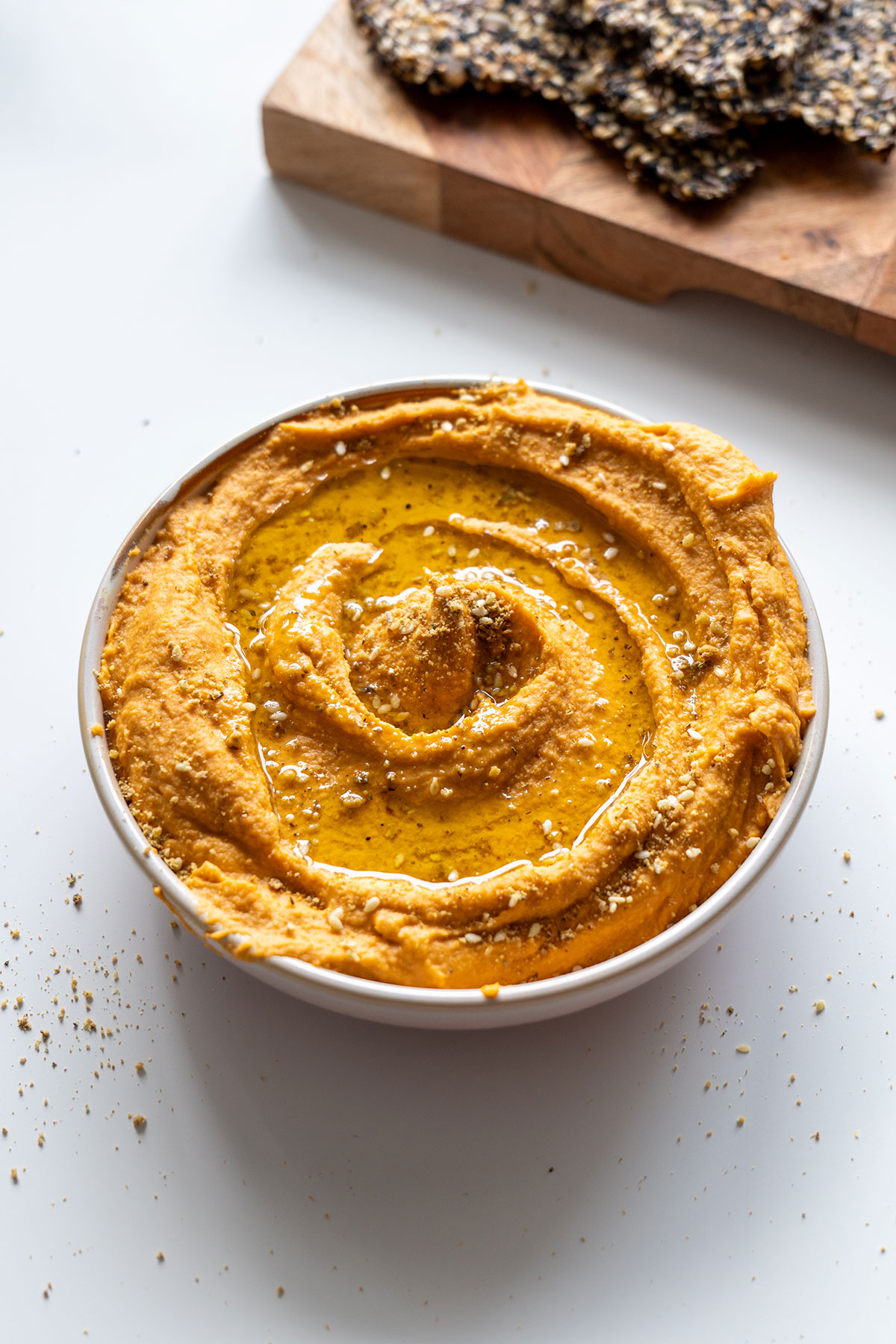 A bowl of red lentil hummus topped with a swirl of olive oil and a sprinkle of toppings such as dukkah, perfect for a nutritious snack.