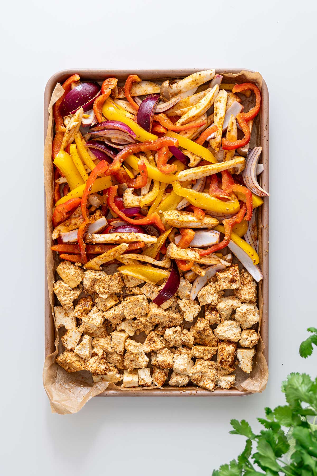 Raw tofu and sliced vegetables seasoned and arranged on a baking sheet, ready to roast.