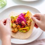 Hands expertly folding a whole grain wrap around the hearty vegan fajita filling