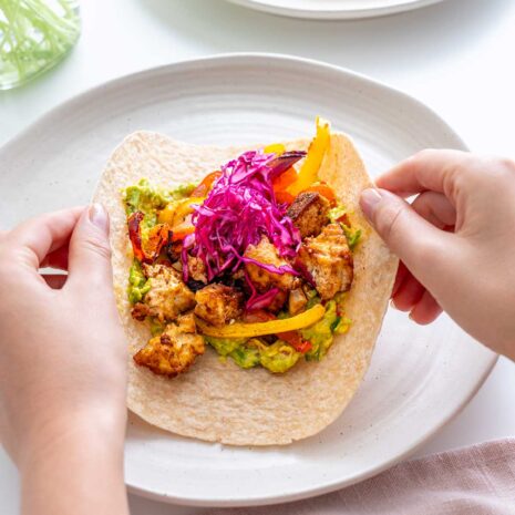 Hands expertly folding a whole grain wrap around the hearty vegan fajita filling