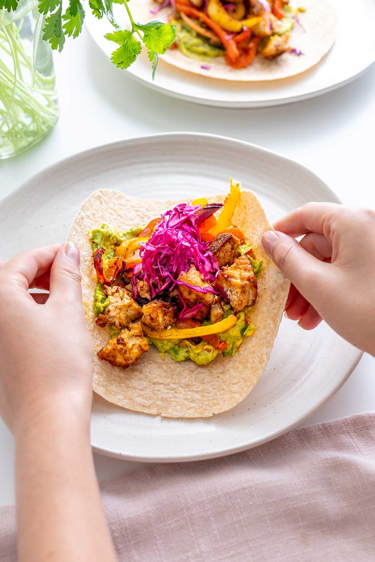 Hands expertly folding a whole grain wrap around the hearty vegan fajita filling