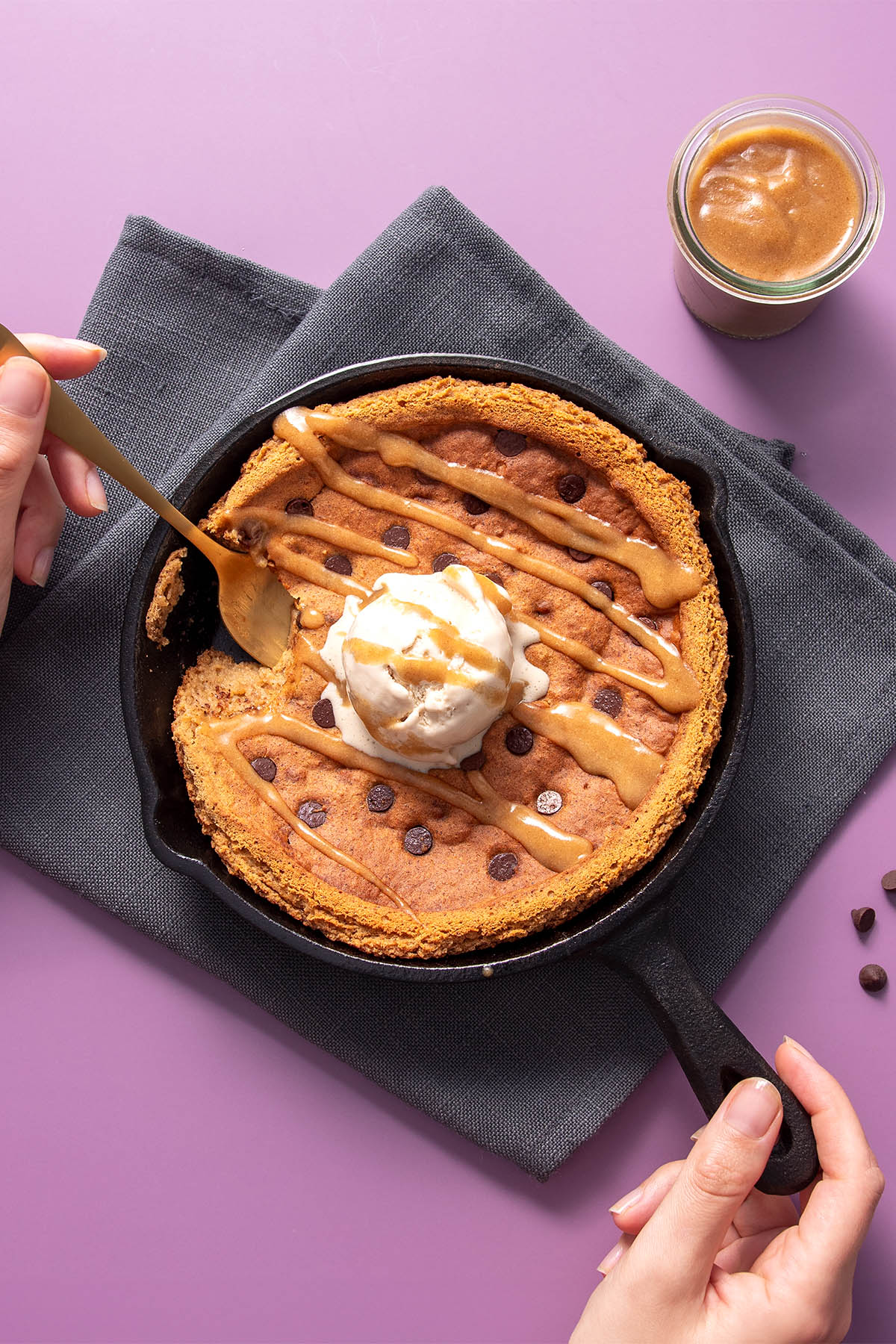 Chickpea blondie skillet on a bright purple background with a delicious jar of sauce on the side.