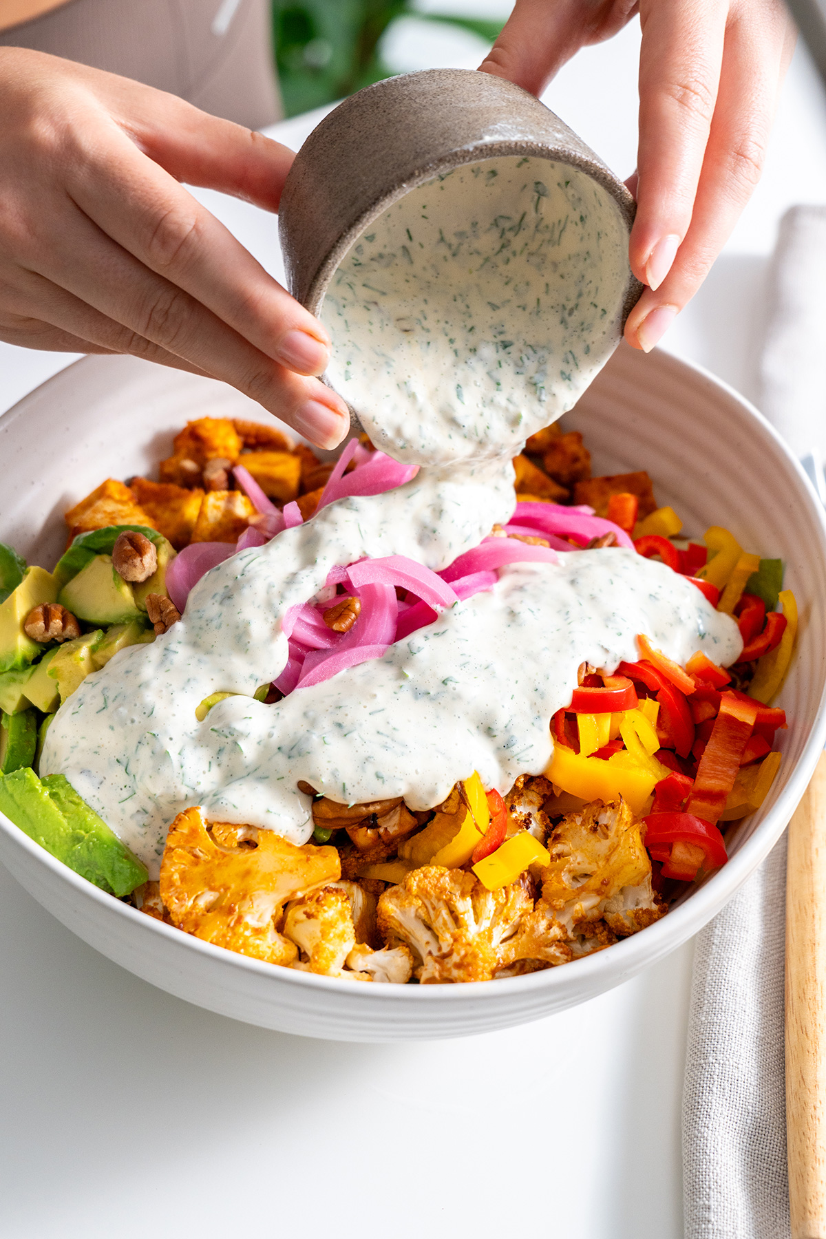 Creamy vegan ranch dressing being poured over a colorful buffalo cauliflower salad.