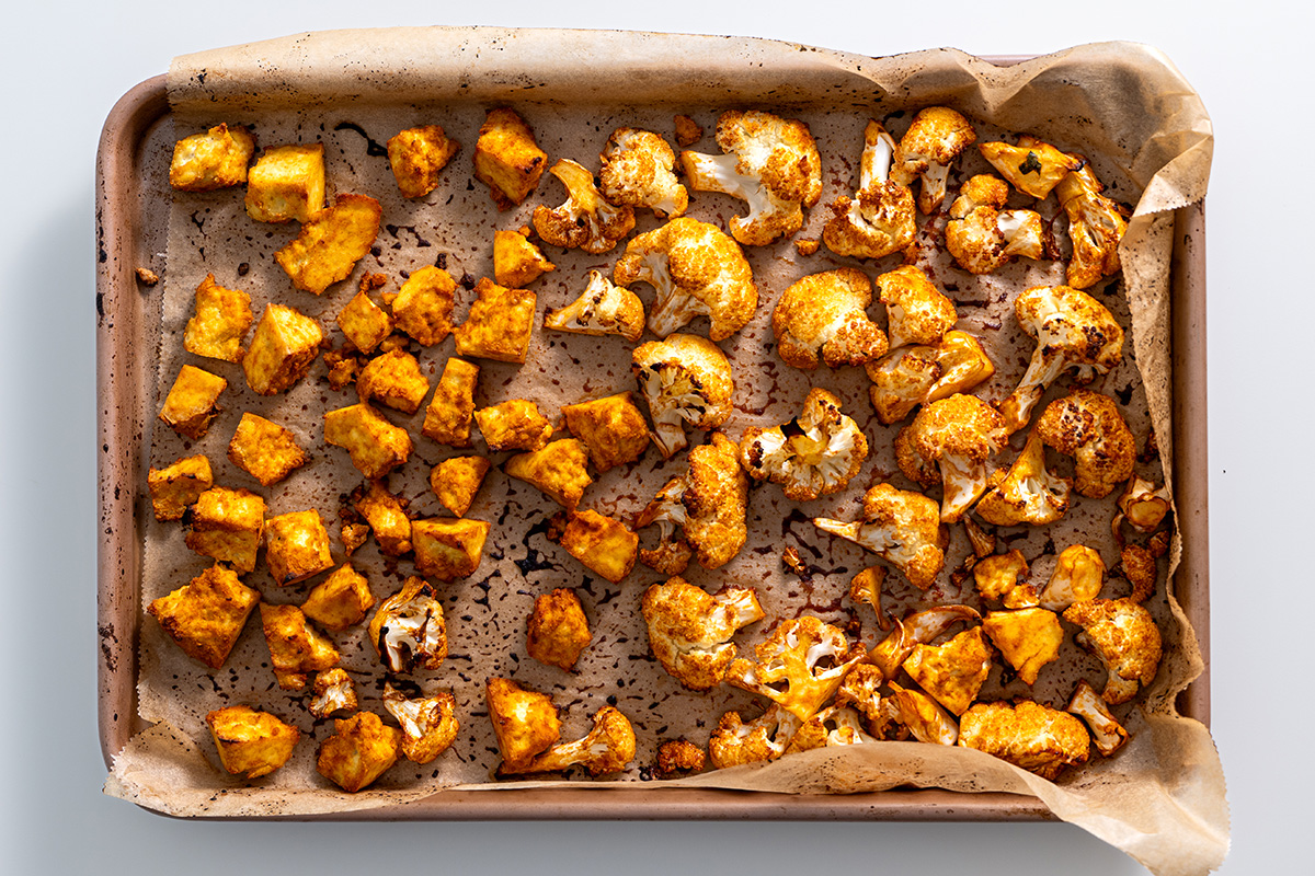 Baked golden-brown buffalo cauliflower florets and tofu on a parchment-lined baking tray.