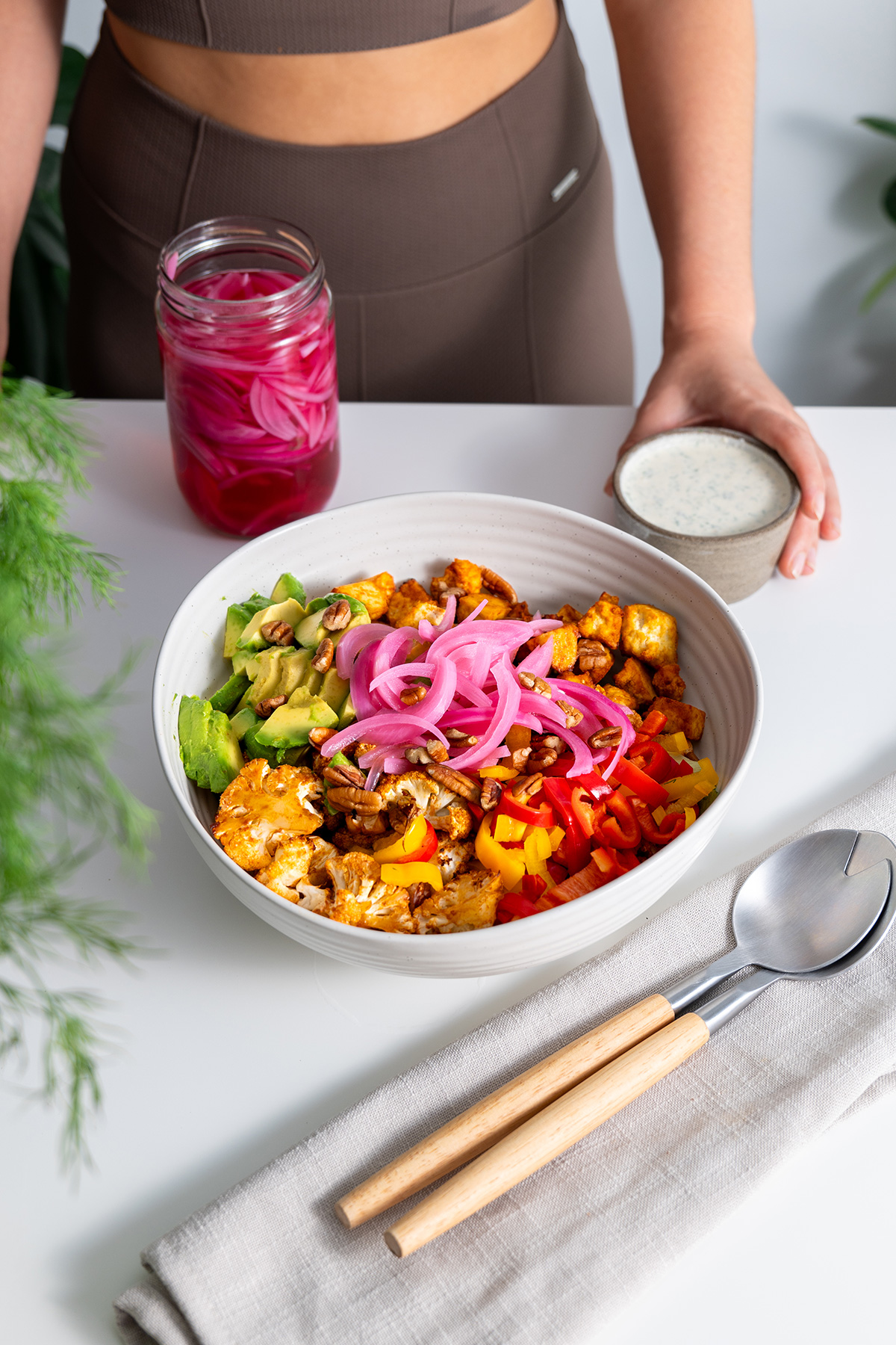Full view of buffalo cauliflower salad with avocado and a tangy, herb-infused ranch dressing with Sarah in the background holding the dressing.