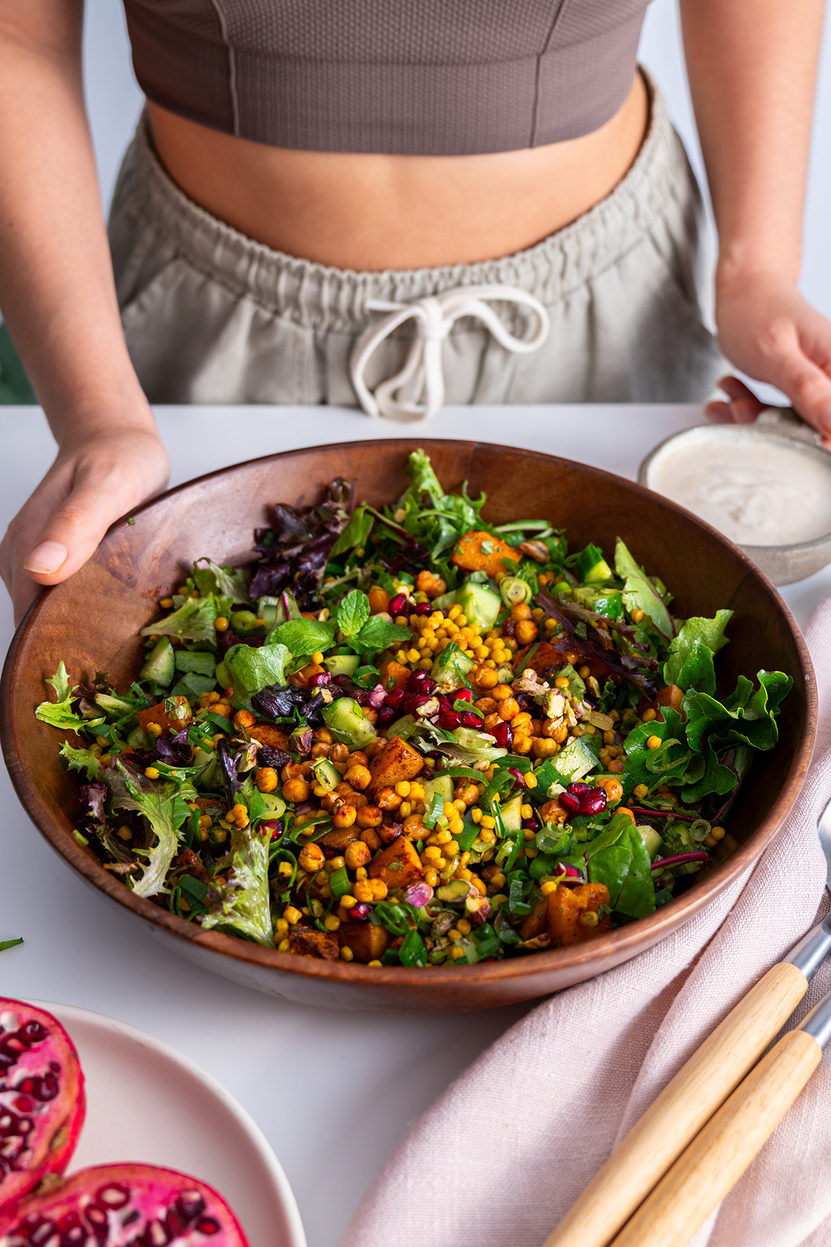Freshly tossed couscous pomegranate salad in a wooden bowl from a front view, ready to add the dressing and serve.