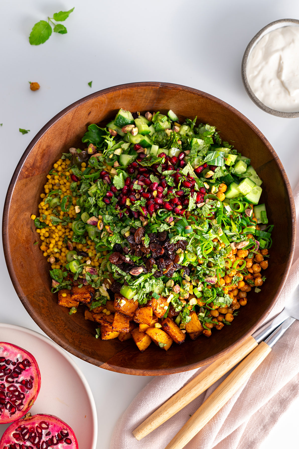 Overhead shot of a wooden bowl filled with a colorful couscous pomegranate salad on a white table.