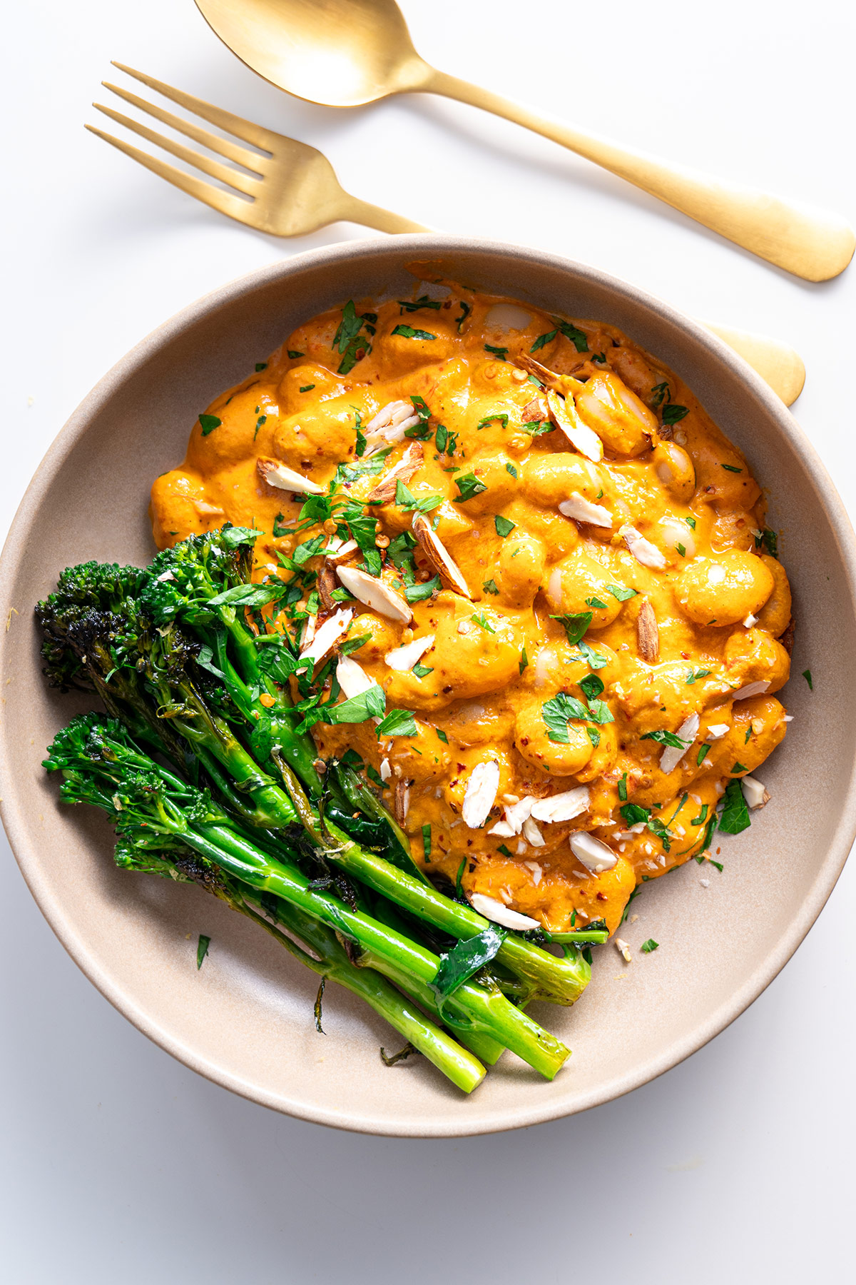 Serving of High-Protein Romesco Butter Beans with garnished parsley and side of broccolini on a clean white background.