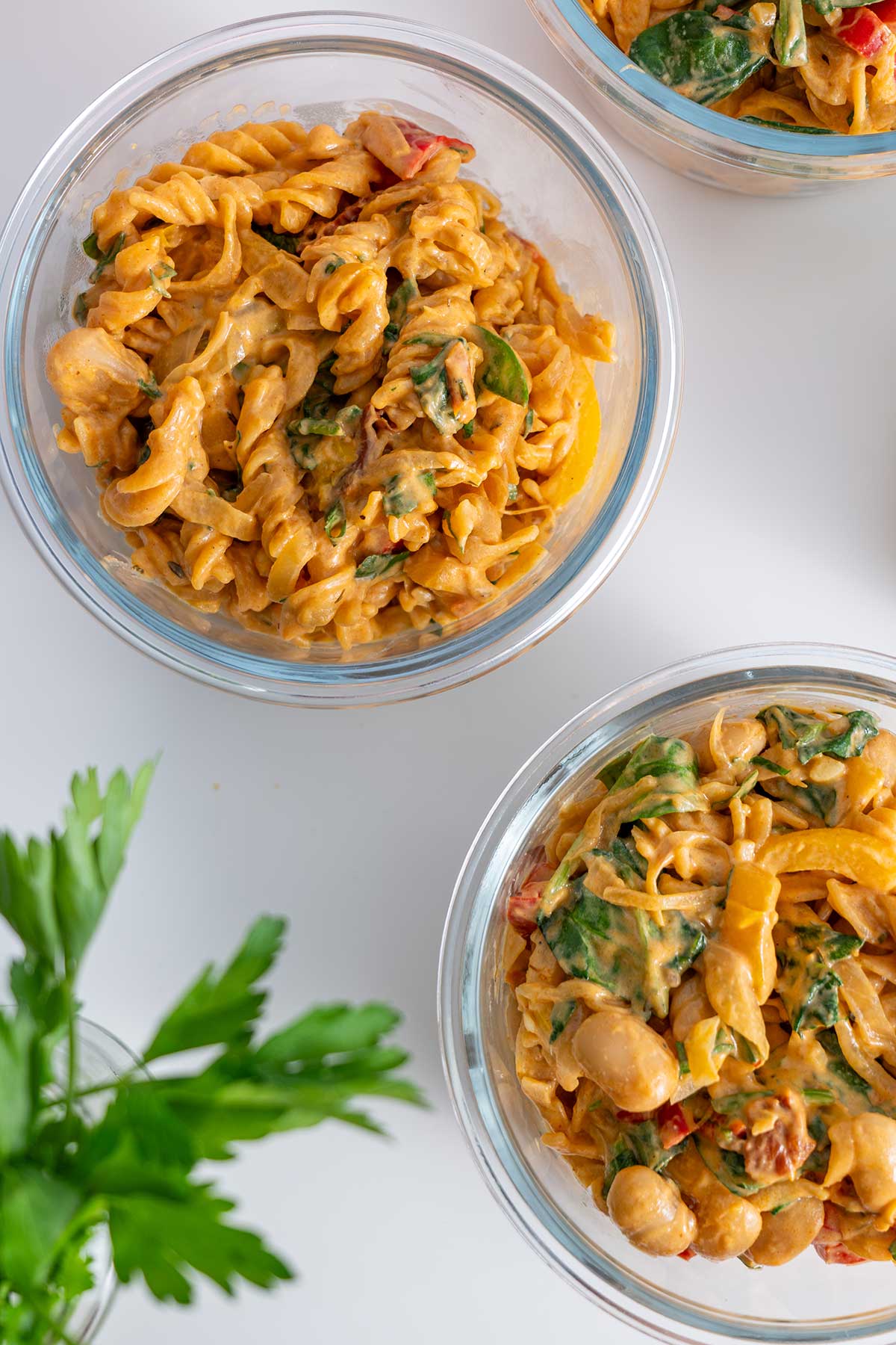 Overhead shot of Meal prep containers ready with servings of 'High-Protein Vegan Marry Me Pasta' on a white counter