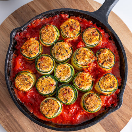 Close-up of Mediterranean zucchini roll-ups in a skillet, showcasing the crispy tops and vibrant tomato sauce.