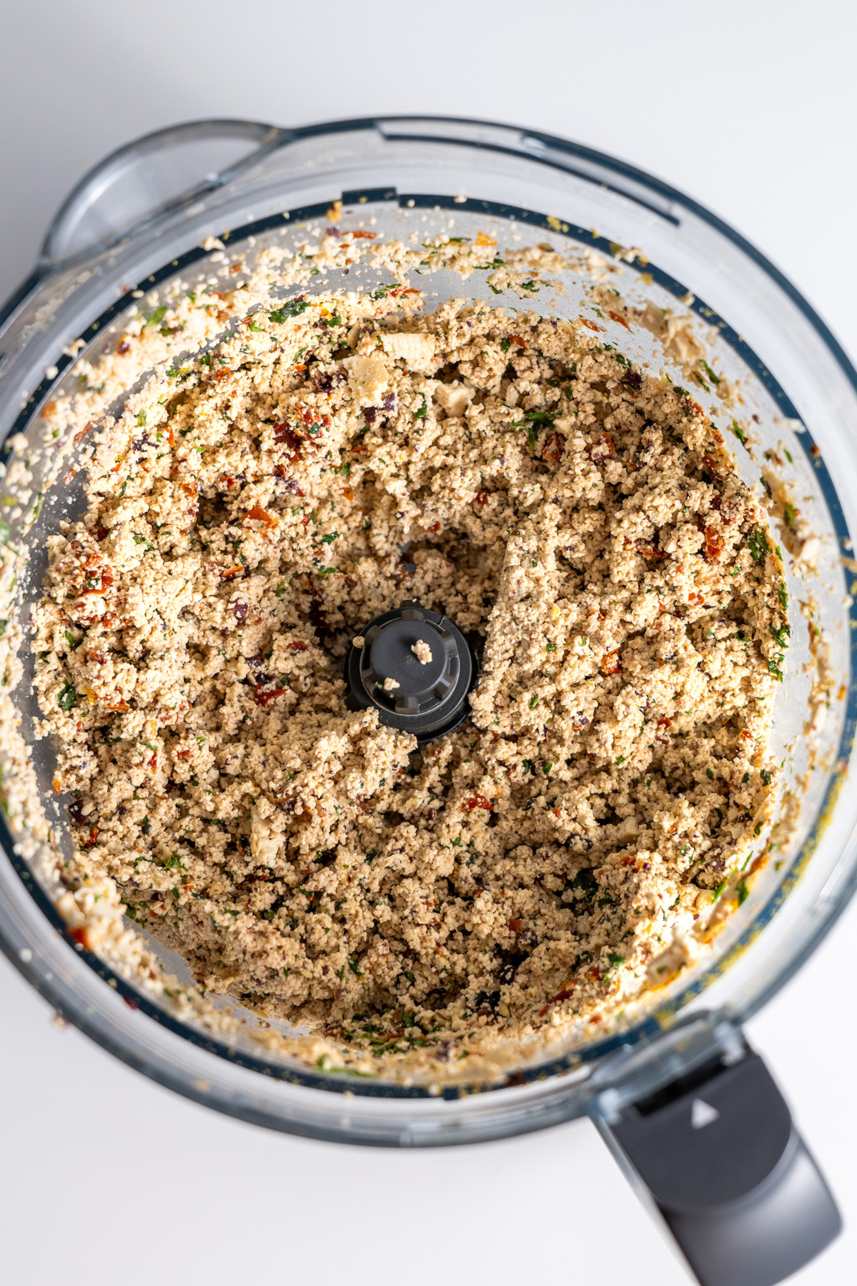 Overhead view of a food processor bowl with a Mediterranean-inspired tofu and vegetable mixture for stuffing zucchini.