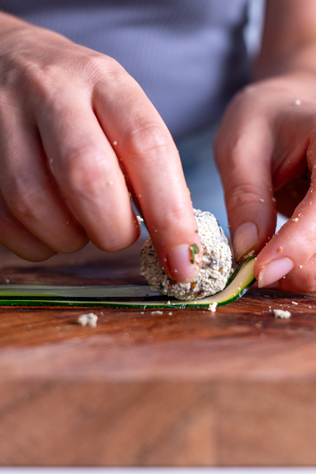 Detailed process of hands rolling a Mediterranean zucchini slice with a tofu and vegetable filling.