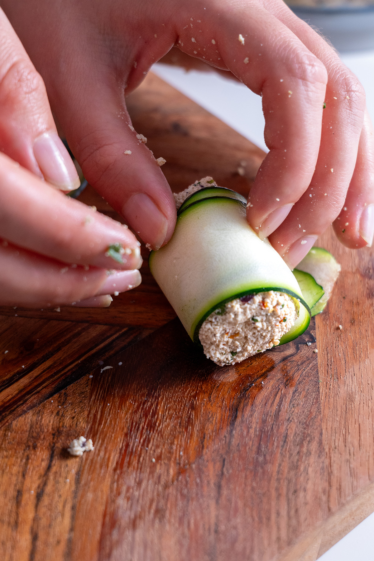 Close-up of hands rolling a Mediterranean zucchini slice filled with a nutritious tofu and herb mixture.