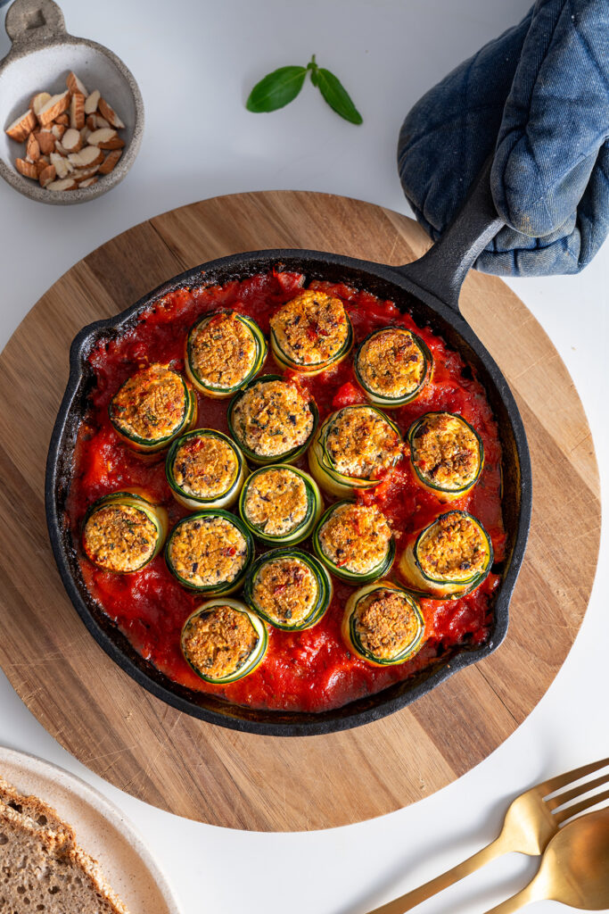 Overhead shot of Mediterranean zucchini roll-ups beautifully arranged in a skillet, served on a light-colored table.