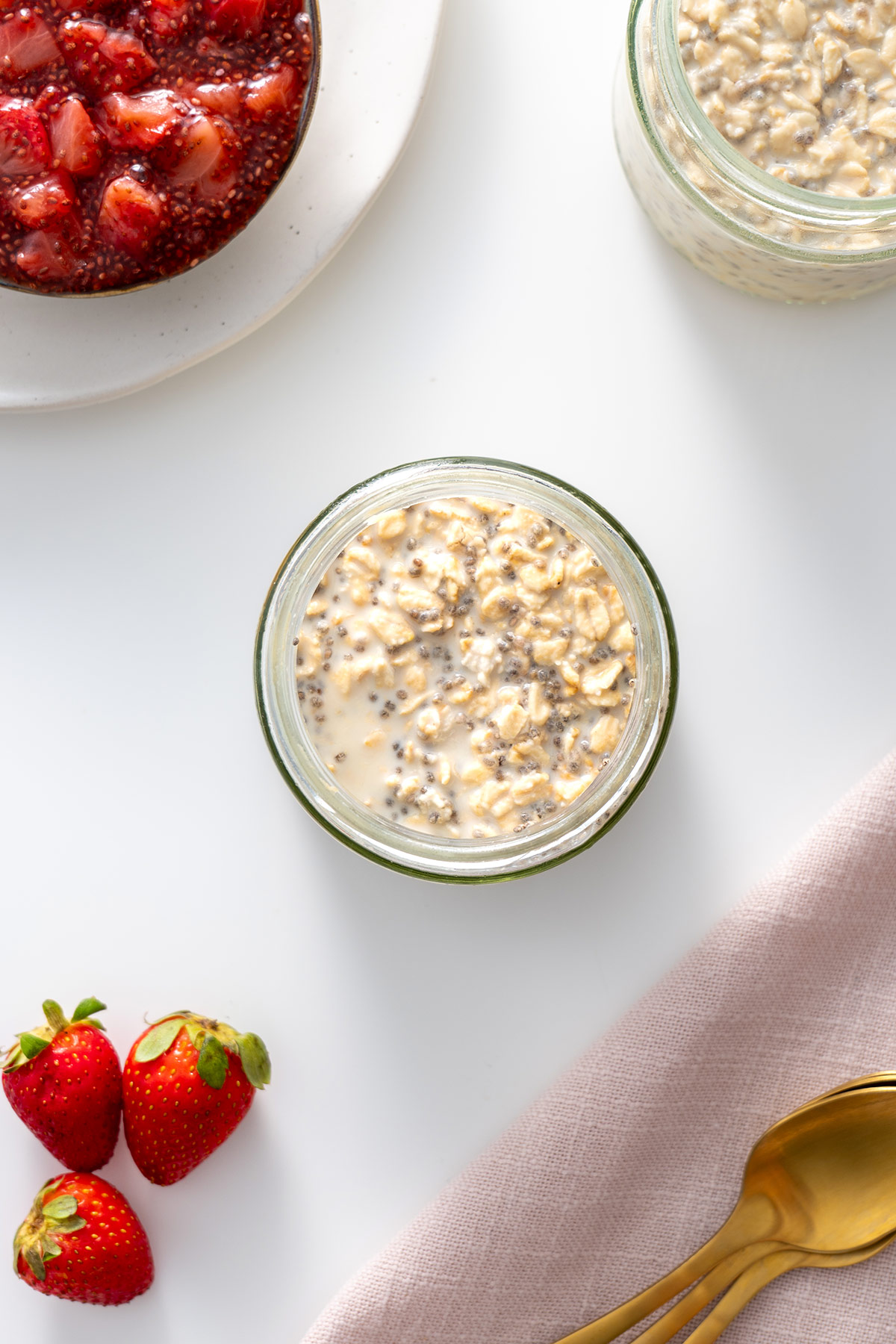 Prepared overnight oats in a jar, with a spoon on the side, next to fresh strawberries, ready for toppings to be added.