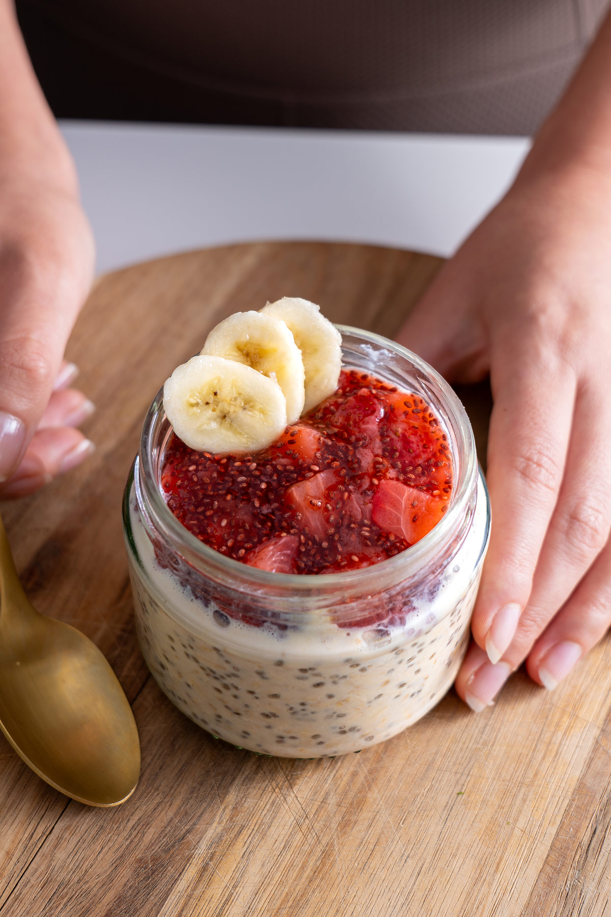 Glass jar of overnight oats layered with strawberry jam, garnished with banana slices and a strawberry fan.