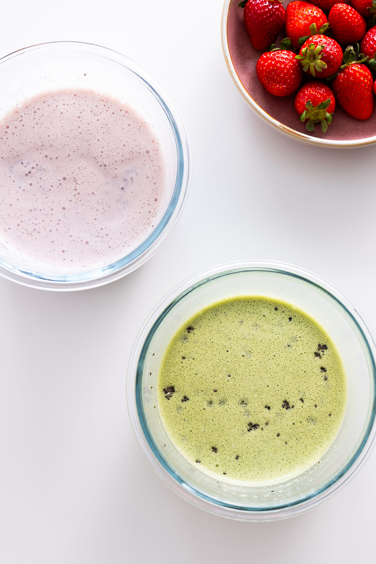 Bowls of matcha and strawberry chia pudding mixture next to fresh strawberries