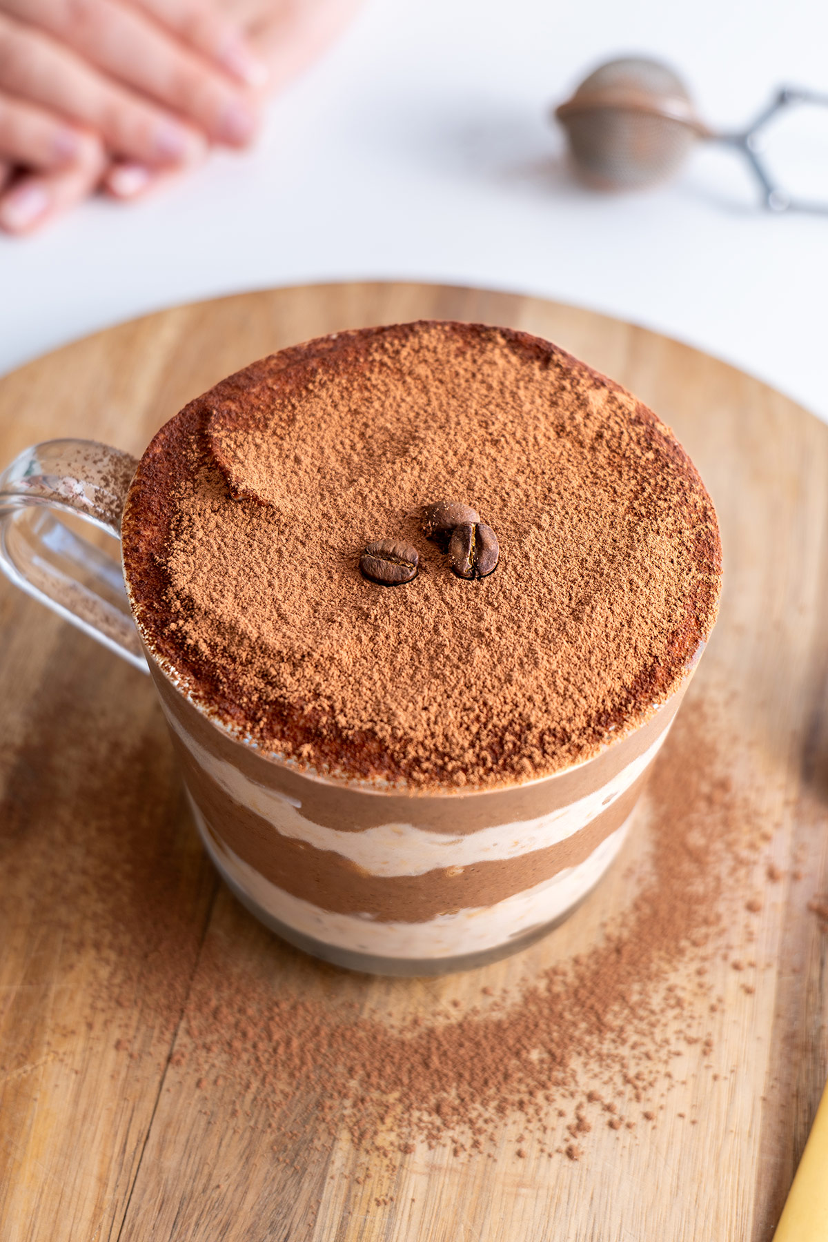 Top view of tiramisu overnight oats in a clear glass on a wooden serving board.