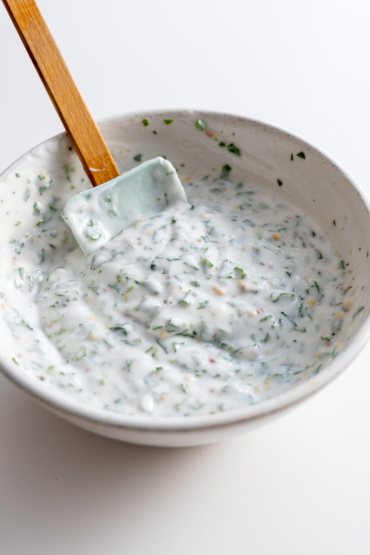 Bowl of creamy herb dressing with a spatula.