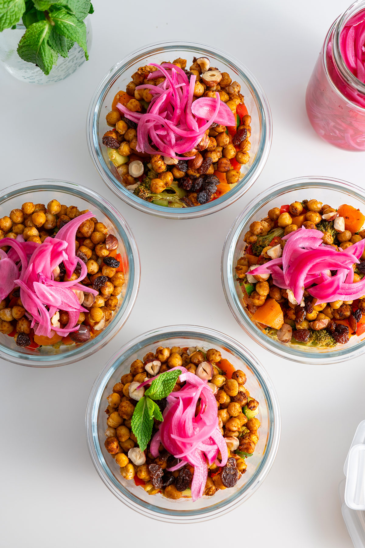 Top view of meal prep containers with couscous and roasted vegetable salad topped with pink pickled onions.