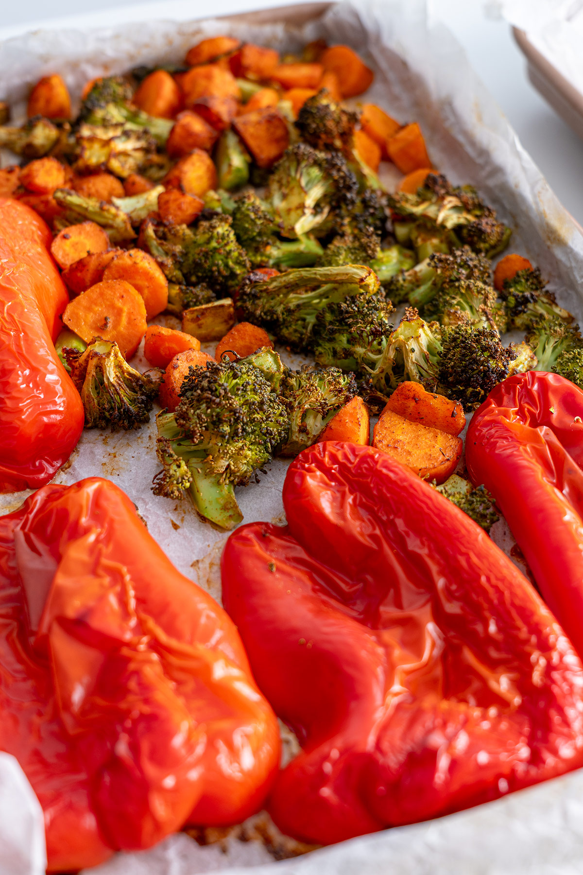 Roasted red peppers, carrots, and broccoli on a baking sheet.