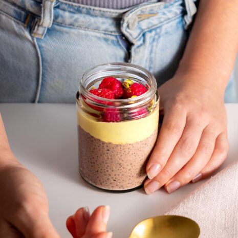 Close-up of a Sarah Cobacho holding a Chocolate Pistachio Chia Pudding in a glass jar, ready to eat.