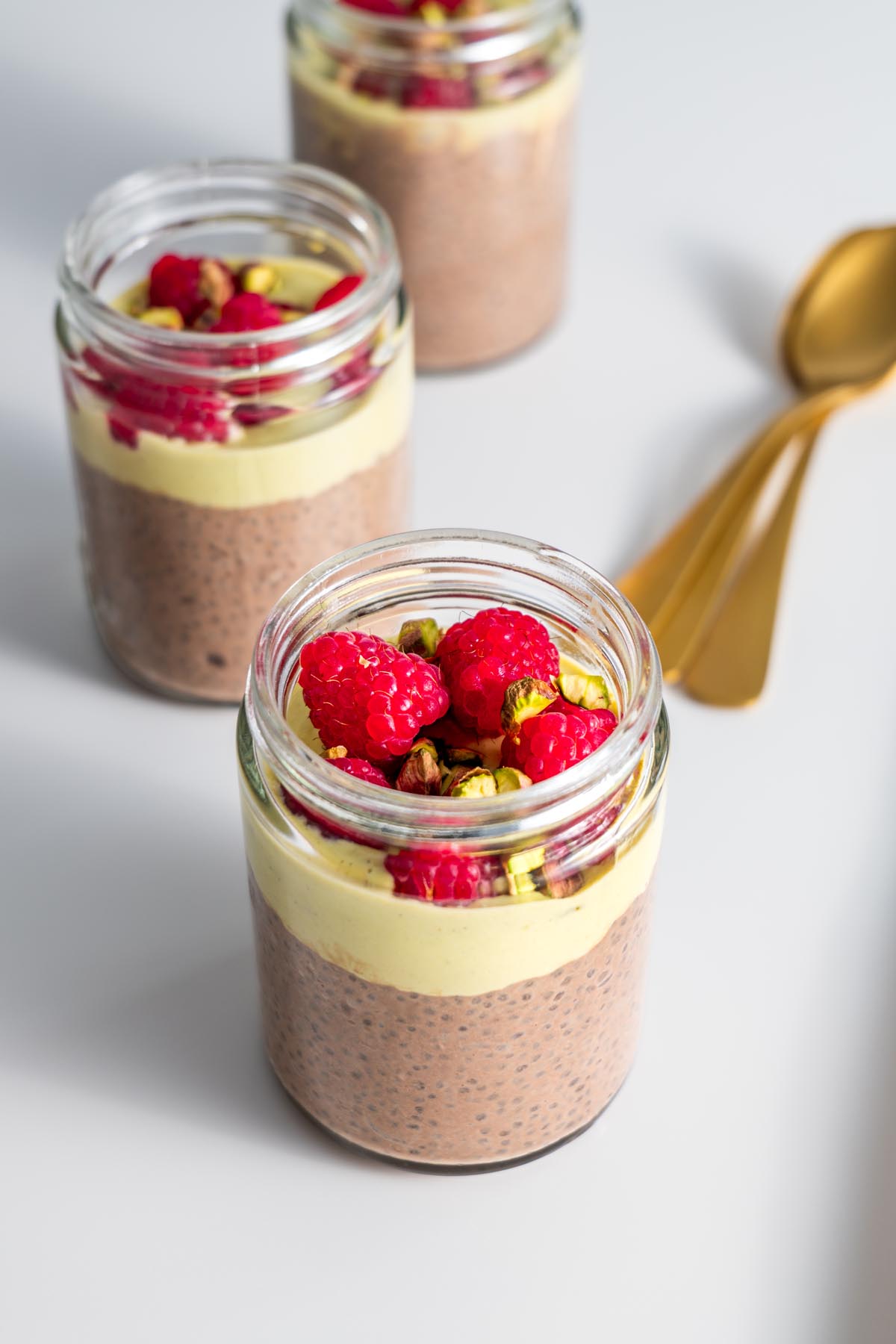 Chocolate Pistachio Chia Pudding in a glass jar, garnished with raspberries and pistachios, on a wooden surface.